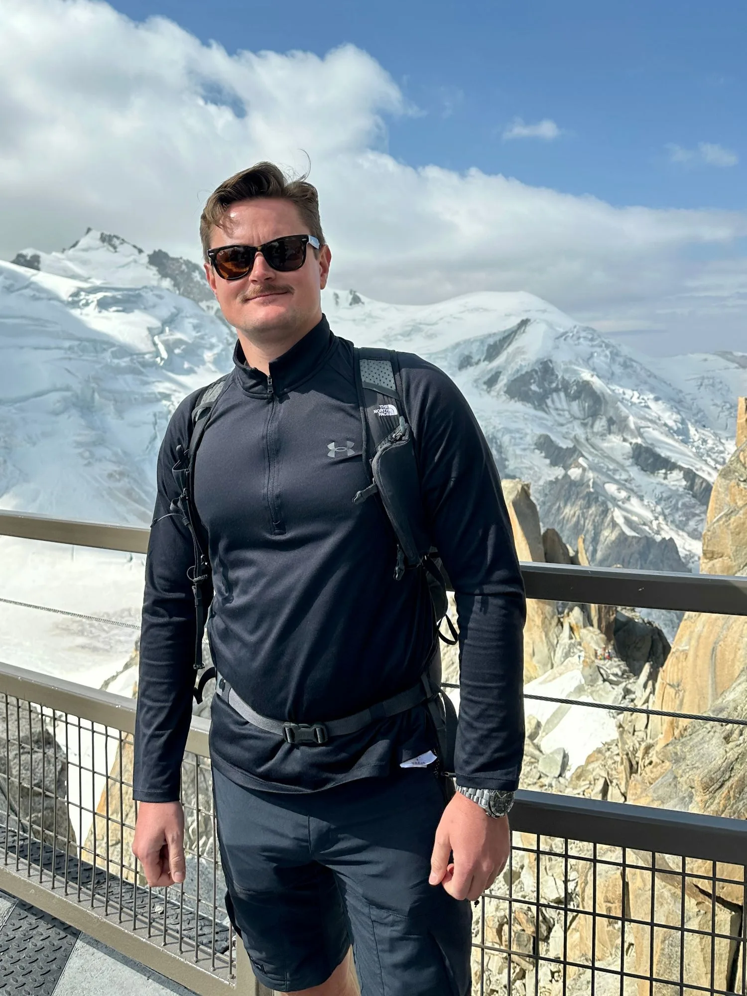 Lennart Böhm on a high-altitude mountain viewing platform, snow-covered peaks in the background.